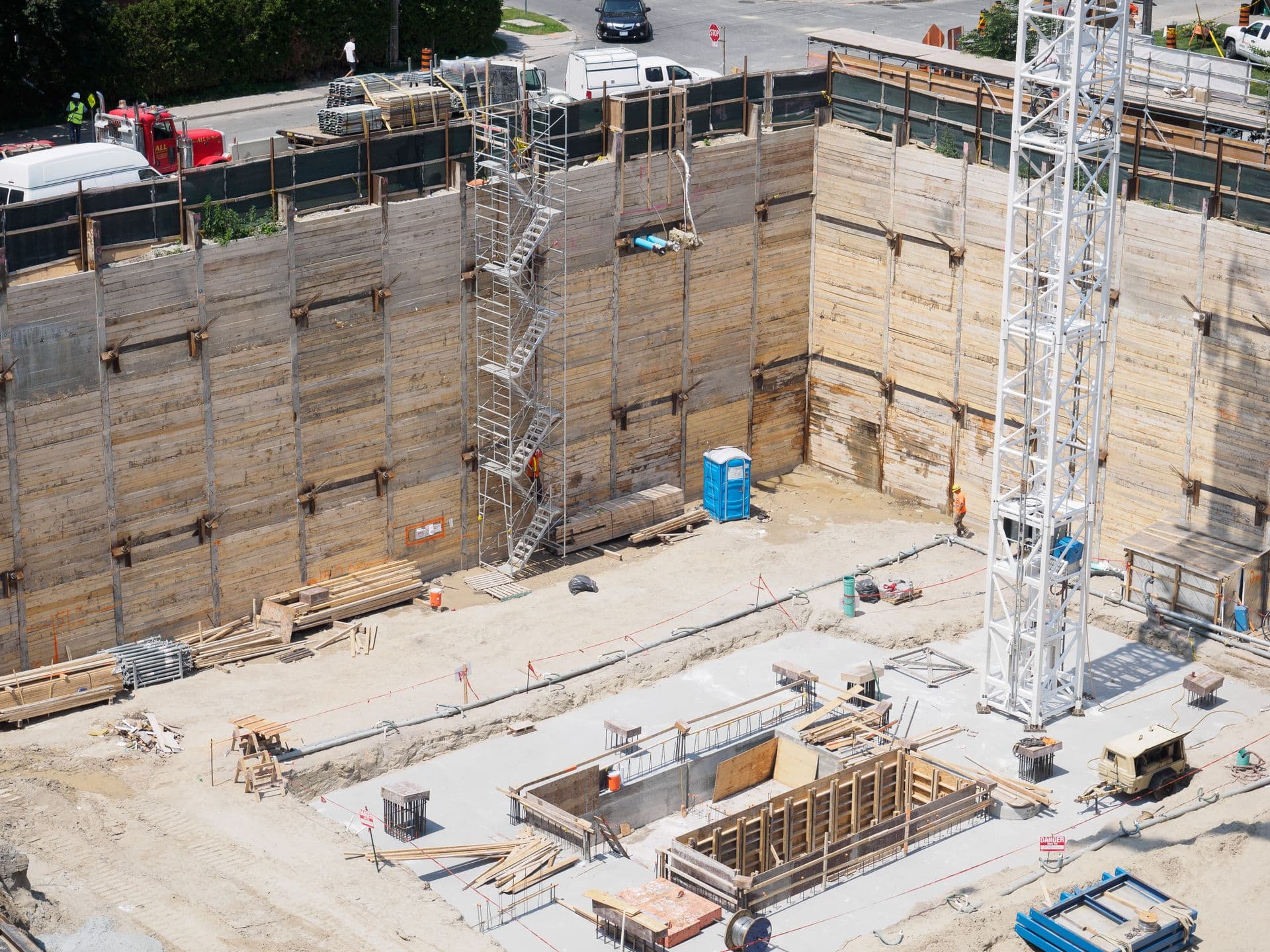 Aerial view of a shored foundation excavation with footing forms and a stair tower